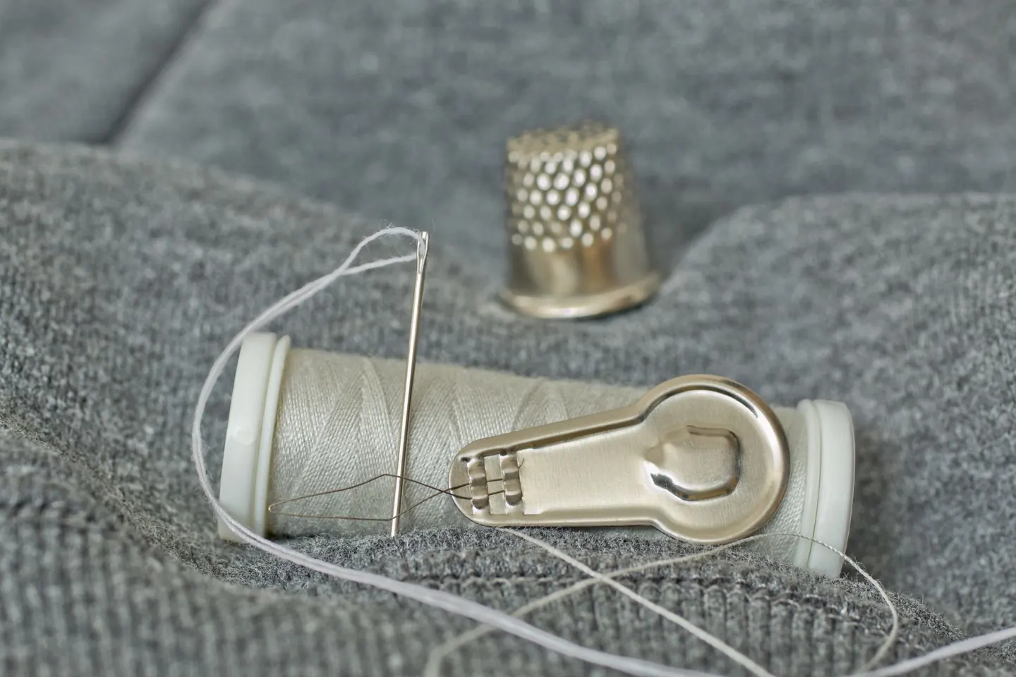 Aiguille, fil et dé à coudre posés sur un tissu gris