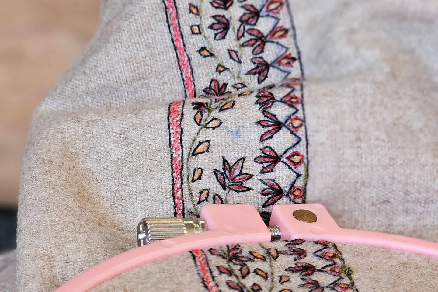 Broderie détaillée sur un tissu beige tendu dans un tambour rose