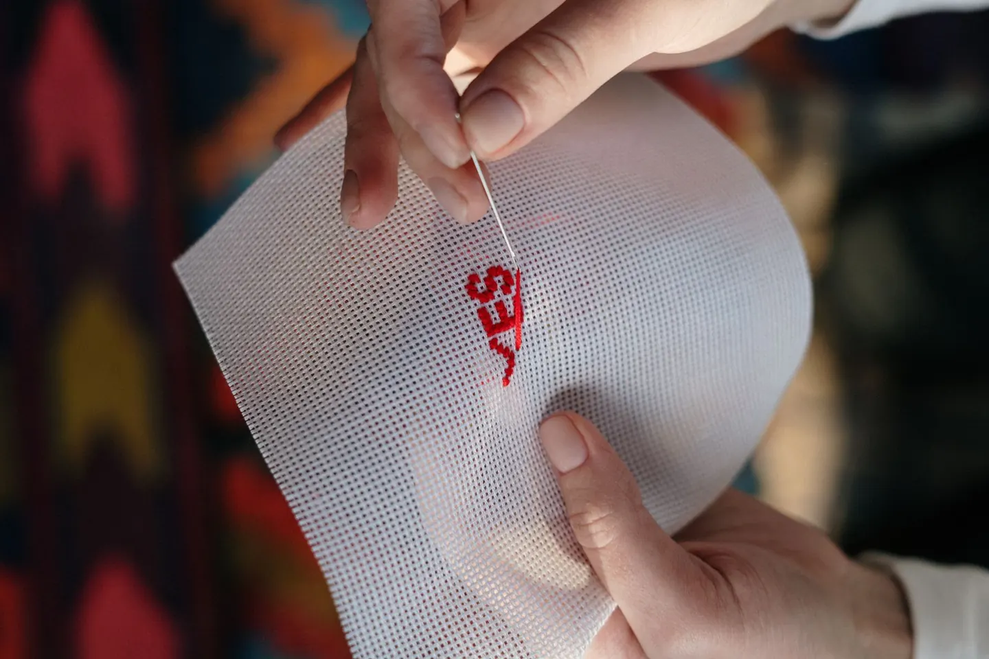 Mains brodant un tissu avec un fil rouge