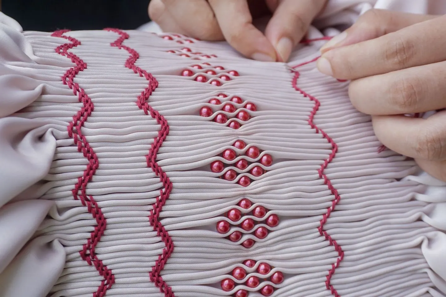 Mains réalisant une broderie décorée de petits éléments en relief